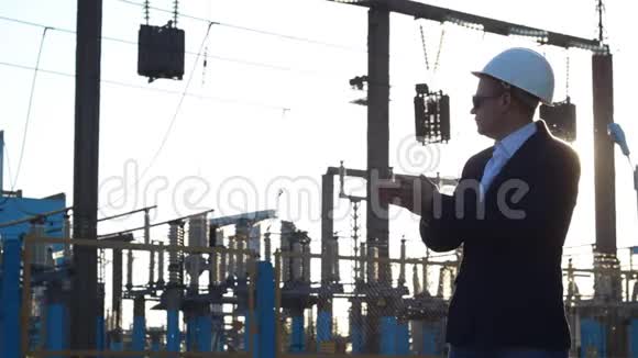 一个戴着白色安全帽和太阳镜的男人在发电厂的背景下搓手日落视频的预览图