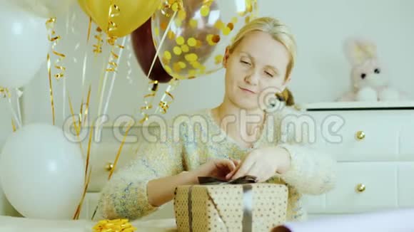 一个女人正在为孩子的生日准备礼物把丝带和蝴蝶结粘在盒子上在孩子们房间里视频的预览图