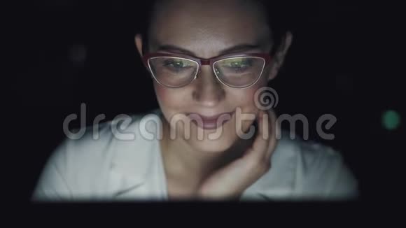 带眼镜的监视器屏幕的反射在办公室工作到很晚的年轻妇女视频的预览图