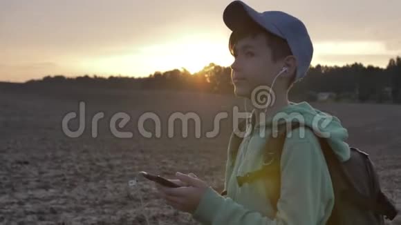 带背包的男孩在日落时走在户外使用电话听音乐旅行的概念视频的预览图