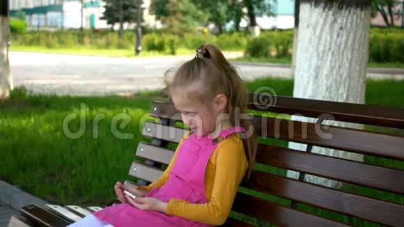 一个学龄前的微笑女孩在公园户外使用电话夏日阳光明媚视频的预览图