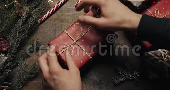 男子手把礼品盒用装饰线绑好后用红纸包在木桌上准备视频的预览图