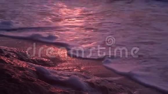 海浪泡沫海浪在潮湿的沙滩上黑暗的大海在橙色日落的背景下视频的预览图