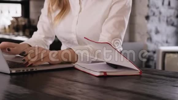 一个白人女孩的特写她的手穿着白色衬衫在笔记本电脑上打字然后写在笔记本上自由职业者视频的预览图