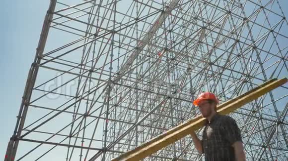 年轻的建筑工人戴着安全帽扛着重金属木板在巨大的装置附近工作视频的预览图