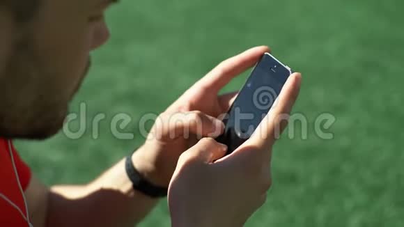 有魅力的男人在球场草坪上听音乐在智能手机上发短信视频的预览图