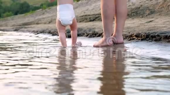 穿尿布的孩子和他母亲沿着河岸走幸福的一家人在海滩上散步慢动作视频的预览图