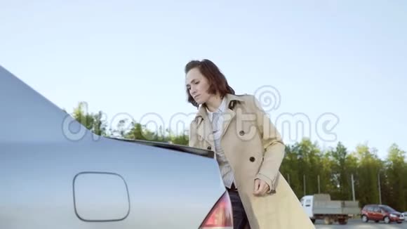 一个穿着米色雨衣的女人打开汽车的后备箱拿出她的手提箱视频的预览图