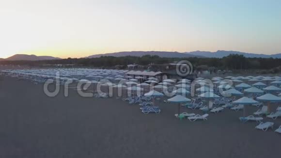 日落时用日光浴床和木伞俯瞰沙滩视频的预览图