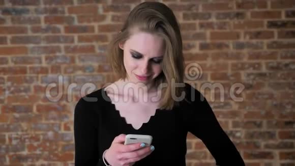 一个眼睛冒烟的年轻女孩正在看智能手机上的照片咯咯地笑着交流理念砖背景视频的预览图