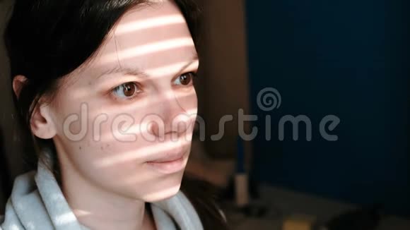 一个黑发女人的特写她的脸上有着窗外的光条视频的预览图