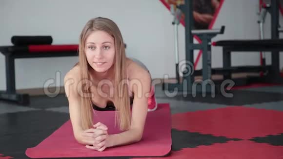 年轻女子在健身房做运动板女孩紧张的肌肉腹部按压视频的预览图