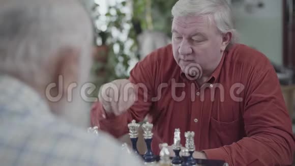 两个坐在家里下棋的高级男子穿红色衬衫的人在动一动白人老人邻居朋友视频的预览图