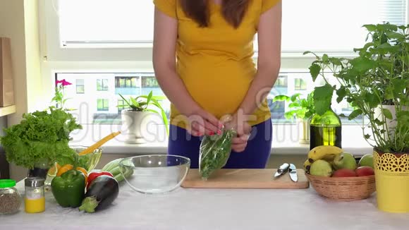 孕妇打开绿色沙拉叶盒放入厨房餐桌上的玻璃菜中视频的预览图