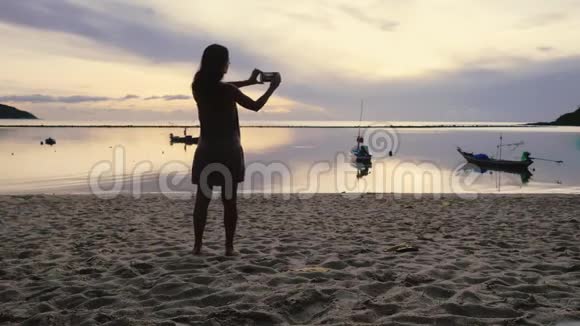 一位年轻女子在热带海滩上用智能手机拍下令人惊叹的日落3840x2160视频的预览图