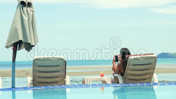 美丽的黑发女人在海滩休息室里用手机洗澡3840x2160视频的预览图