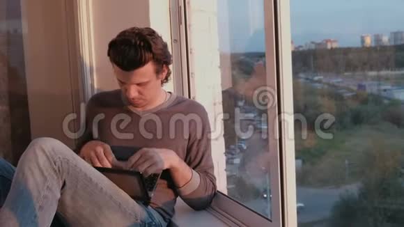 傍晚日落时分疲惫的男人坐在阳台上的笔记本电脑上工作视频的预览图
