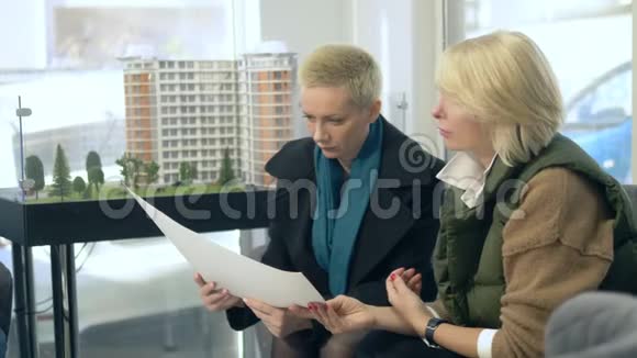 两个女人正在说话坐在售楼处的背景上布置着大楼视频的预览图