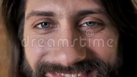 带着胡子的年轻黑发男子的眼睛正在镜头前看着微笑着带着砖的背景视频的预览图