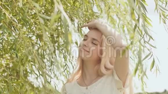 年轻的俄罗斯女孩金发碧眼在柳枝的背景下摆姿势视频的预览图