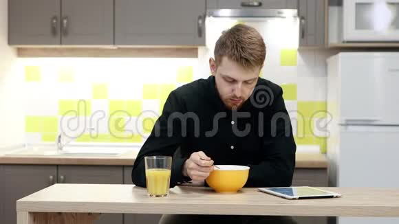 带着平板电脑的年轻人坐在厨房的桌子旁吃早餐视频的预览图