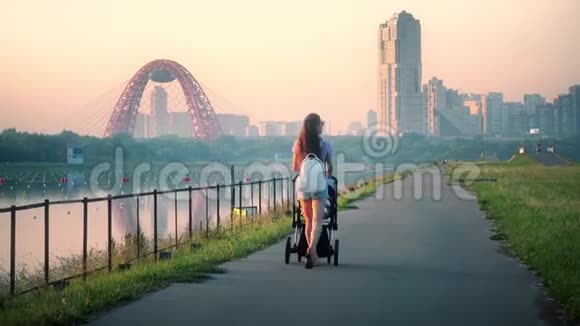 傍晚年轻女子推着婴儿车来到远处的城市景观视频的预览图