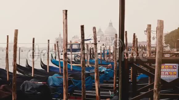 意大利威尼斯雾蒙蒙的木制码头上传统的意大利贡多拉斯在海浪中摇摆背景是古老的建筑视频的预览图