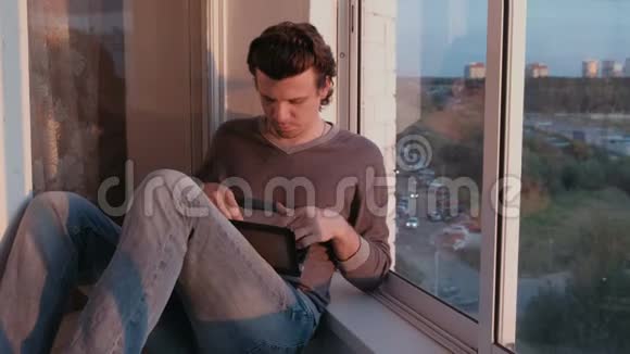 傍晚日落时分疲惫的男人坐在阳台上的笔记本电脑上工作视频的预览图