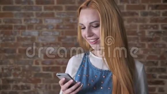 年轻迷人的金发女孩正在智能手机上阅读信息微笑砖背景交流理念视频的预览图