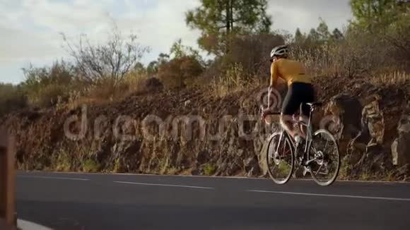 一个戴着头盔和运动装备的职业自行车手在日落时分骑在蜿蜒的山上朝视频的预览图