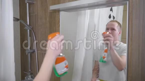 一个人打扫浴室里的镜子一个年轻人用纸巾清洁浴室镜子一个人洒在视频的预览图