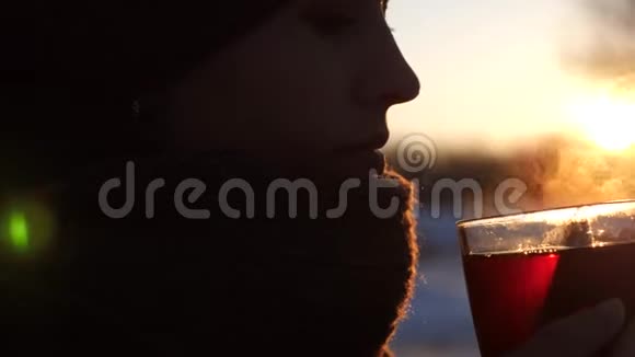 美丽的冷冻女孩喝茶从透明的玻璃户外在眩目的夕阳视频的预览图