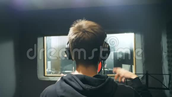 男歌手戴耳机在音响室唱歌无法辨认的年轻人情绪录制歌曲工作视频的预览图