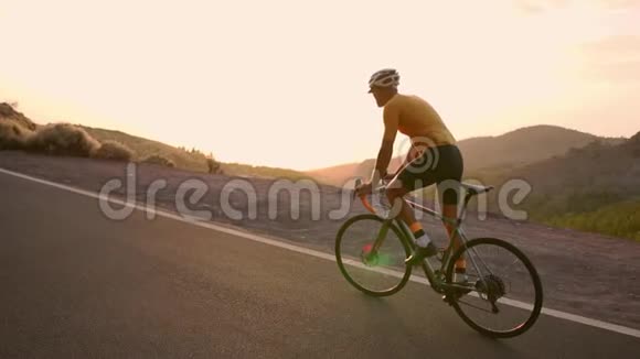 一个戴着头盔和运动装备的专业骑自行车的人在日落时缓慢地骑在山区公路上Stadicam视频的预览图