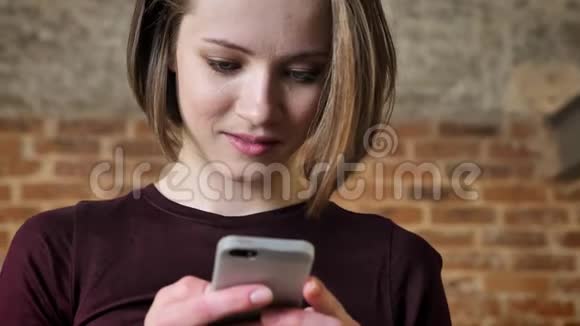 年轻漂亮的女孩正在智能手机上阅读信息她感到惊讶沟通观念砖背景视频的预览图
