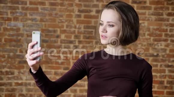 年轻漂亮的女孩有她的智能手机视频通话沟通概念砖背景视频的预览图