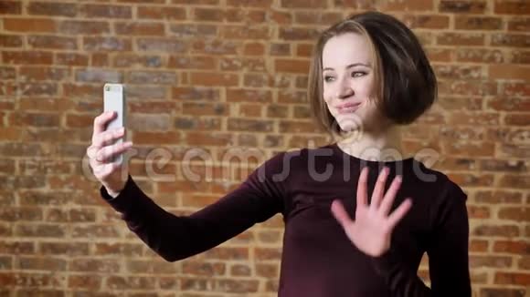 年轻漂亮的女孩有视频通话她的智能手机微笑沟通概念砖背景视频的预览图