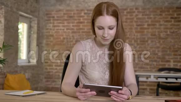 年轻可爱的生姜女孩在她的平板电脑上显示绿色屏幕在相机上观看交流理念砖块视频的预览图