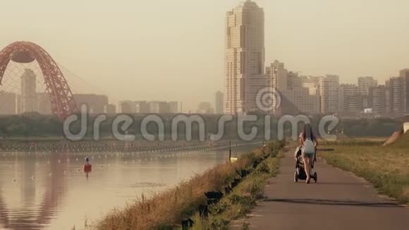 年轻女子推着婴儿车沿着海滨小路穿过城市景观视频的预览图