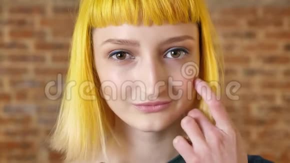 现代青年黄色头发的年轻女子对着镜头微笑美女肖像砖背景视频的预览图