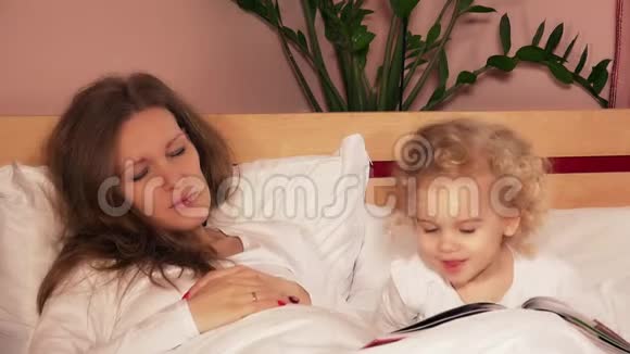 爱可爱的女儿女孩和她的母亲接吻试图睡在白色的床上视频的预览图
