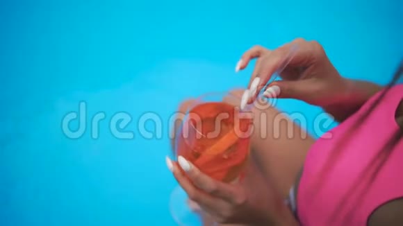 漂亮性感的女孩穿着泳衣在游泳池旁喝鸡尾酒放松慢动作视频的预览图