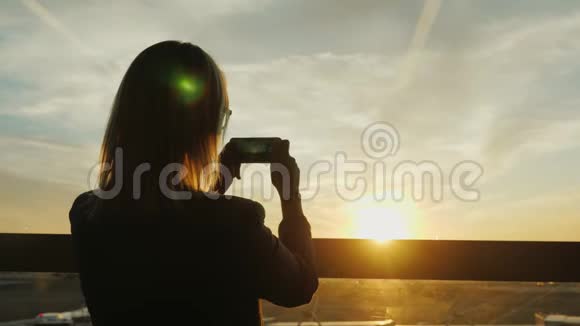 一个穿西装的女人在窗户里拍一张日落的照片在办公楼或机场候机楼视频的预览图