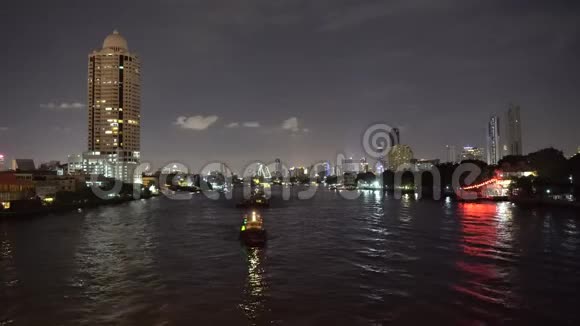 市中心的河夜景摩天大楼的灯光和船只沿着河游视频的预览图