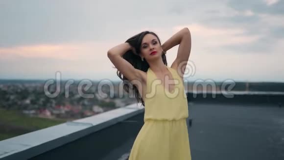 一个穿黄色衣服的女孩在屋顶上跳舞和摆姿势在背景蓝天和屋顶的房子视频的预览图