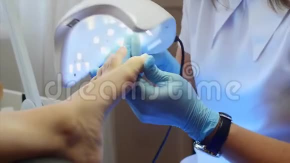 带手套的教育学大师正在用特殊的紫外线灯在脚趾上干燥紫胶视频的预览图