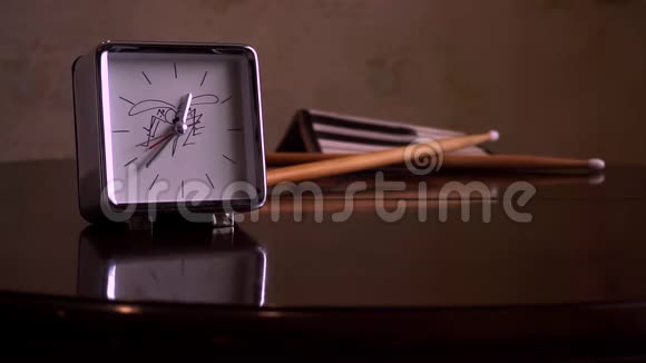 在一张光滑的棕色木桌上有一个反光有一个白色表盘一个钟和鼓棒的方形银视频的预览图