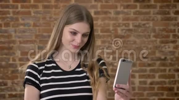 年轻快乐的金发女郎在智能手机上的视频聊天中交谈交流概念砖背景视频的预览图