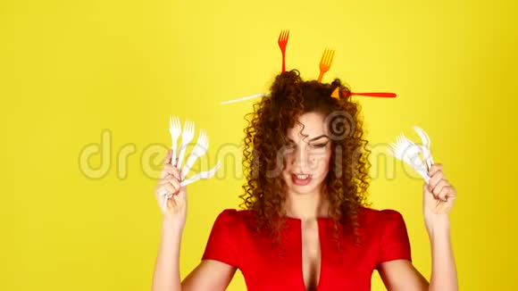 年轻漂亮的女人穿着黄色背景的红色连衣裙头发上有塑料叉子的女性肖像环境视频的预览图
