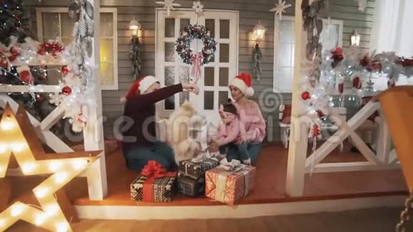 一家人带着小女儿和狗坐在门廊和圣诞树微笑视频的预览图